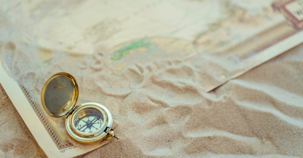 A close-up of a vintage compass on sand with a map, symbolizing travel and exploration.